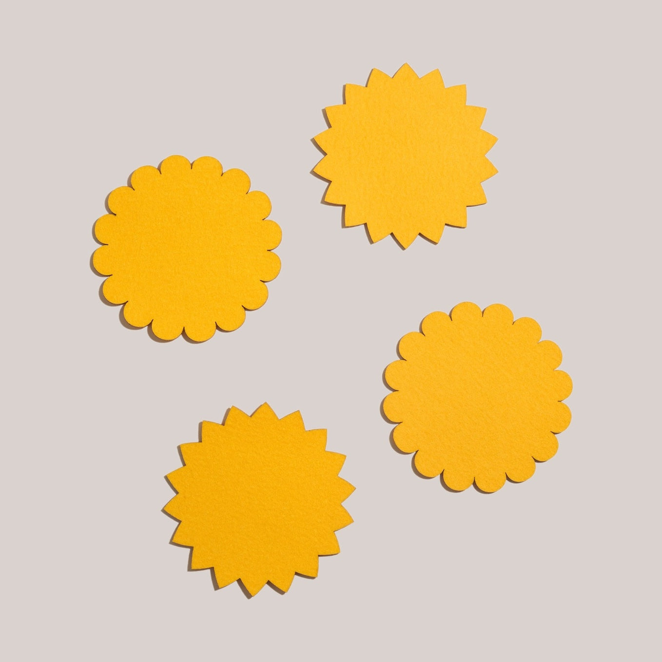 A set of yellow Sunburst Felt Cocktail Napkins spread out on a white seamless background.