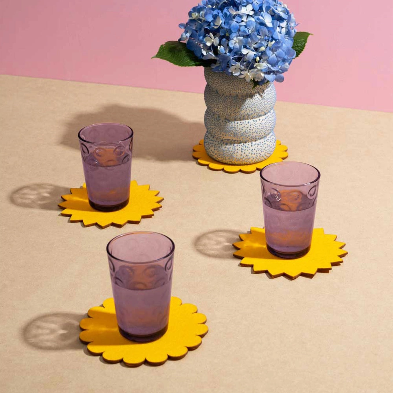 Purple glassware and flower vase on top of 4 yellow Sunburst Felt Cocktail Napkins.