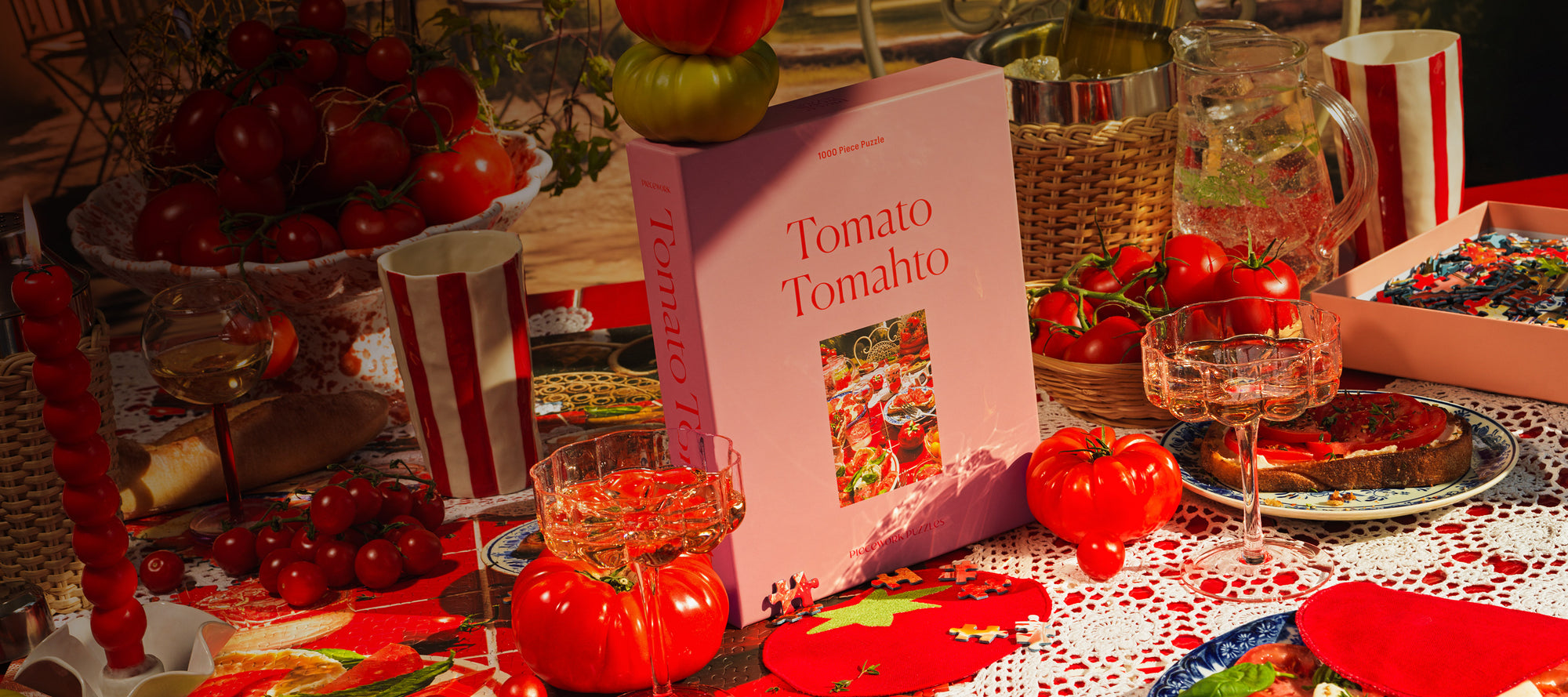 A vibrant tomato-themed tablescape featuring Piecework's Tomato Tomahto 1000-piece puzzle, fresh tomatoes, elegant glassware, and playful red picnic-inspired decor—perfect for foodies, puzzle enthusiasts and, of course, tomato lovers.