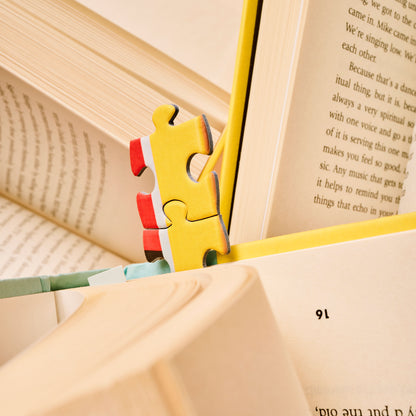 A puzzle piece from Bookworm, a 500-Piece Puzzle from Piecework Puzzles, sticking out of a book like a bookmark.